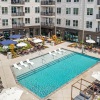  A large swimming pool surrounded by lounge chairs and umbrellas in front of a multi-story apartment building.