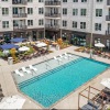  A large swimming pool surrounded by lounge chairs and umbrellas in front of a multi-story apartment building.